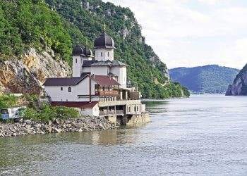 white and black house located at riverside on mountain slope at daytime