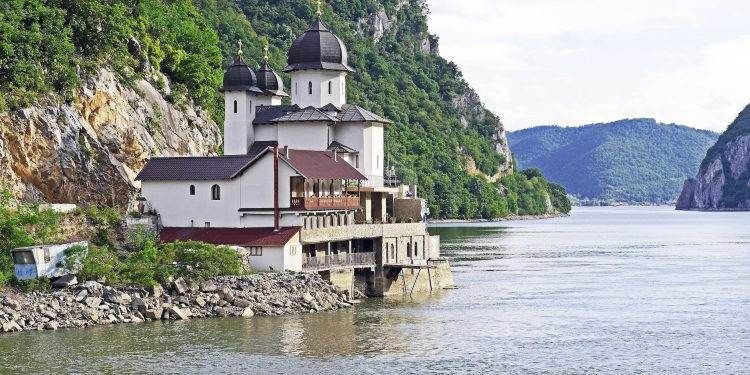 white and black house located at riverside on mountain slope at daytime