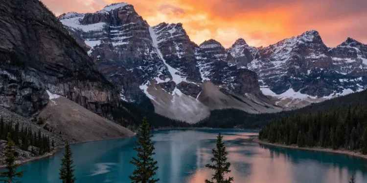 A panoramic view of the Rocky Mountains in Canada at sunset, with snow-capped peaks reflecting in a turquoise lake (Moraine Lake), pine trees in the foreground, vibrant orange and pink sky, photorealistic style, high detail, dramatic lighting.