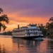A majestic paddlewheel steamboat cruising on the Mississippi River at sunset, with ancient oak trees draped in Spanish moss lining the riverbanks, against a vibrant orange and purple sky, hyper-realistic photography style, detailed reflections on water, National Geographic quality