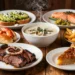 A colorful and appetizing collage of iconic North American dishes arranged on a rustic wooden table. In the foreground, a plate of Texas BBQ beef brisket with smoke rings, next to a bowl of New England clam chowder, a lobster roll, a slice of pecan pie, and a poutine with cheese curds. In the background, soft blurred images of a California avocado toast and a Pacific Northwest salmon fillet. Warm lighting, cinematic style, high detail, food photography aesthetic.