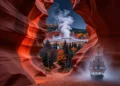 A mystical, cinematic landscape of North America blending diverse iconic elements: a glowing red Antelope Canyon slot canyon with light beams, a dark autumnal forest path near Salem, steam from a Yellowstone geyser in the background, and the ghostly silhouette of a sailing ship in fog over Newfoundland, all seen through a dreamlike, ethereal atmosphere, with a subtle starry night sky, digital art, high detail, dramatic lighting