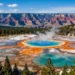 A panoramic view of majestic North American landscapes: in the foreground, a crystal-clear lake with turquoise water (like Lake Louise) surrounded by pine forests and snow-capped Rocky Mountains; in the midground, a geothermal spring with bright orange and blue colors (like Grand Prismatic Spring); in the background, a deep canyon with red rock layers (like Grand Canyon). The sky is clear blue with a few soft clouds. Photorealistic style, high detail, vibrant colors, wide angle, no people.