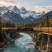 A scenic train journey through the Rocky Mountains in Canada, with a vintage steam locomotive crossing a high trestle bridge over a turquoise river, surrounded by snow-capped peaks and dense pine forests, golden hour light, photorealistic style, wide angle view.