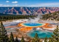 A panoramic view of majestic North American landscapes: in the foreground, a crystal-clear lake with turquoise water (like Lake Louise) surrounded by pine forests and snow-capped Rocky Mountains; in the midground, a geothermal spring with bright orange and blue colors (like Grand Prismatic Spring); in the background, a deep canyon with red rock layers (like Grand Canyon). The sky is clear blue with a few soft clouds. Photorealistic style, high detail, vibrant colors, wide angle, no people.